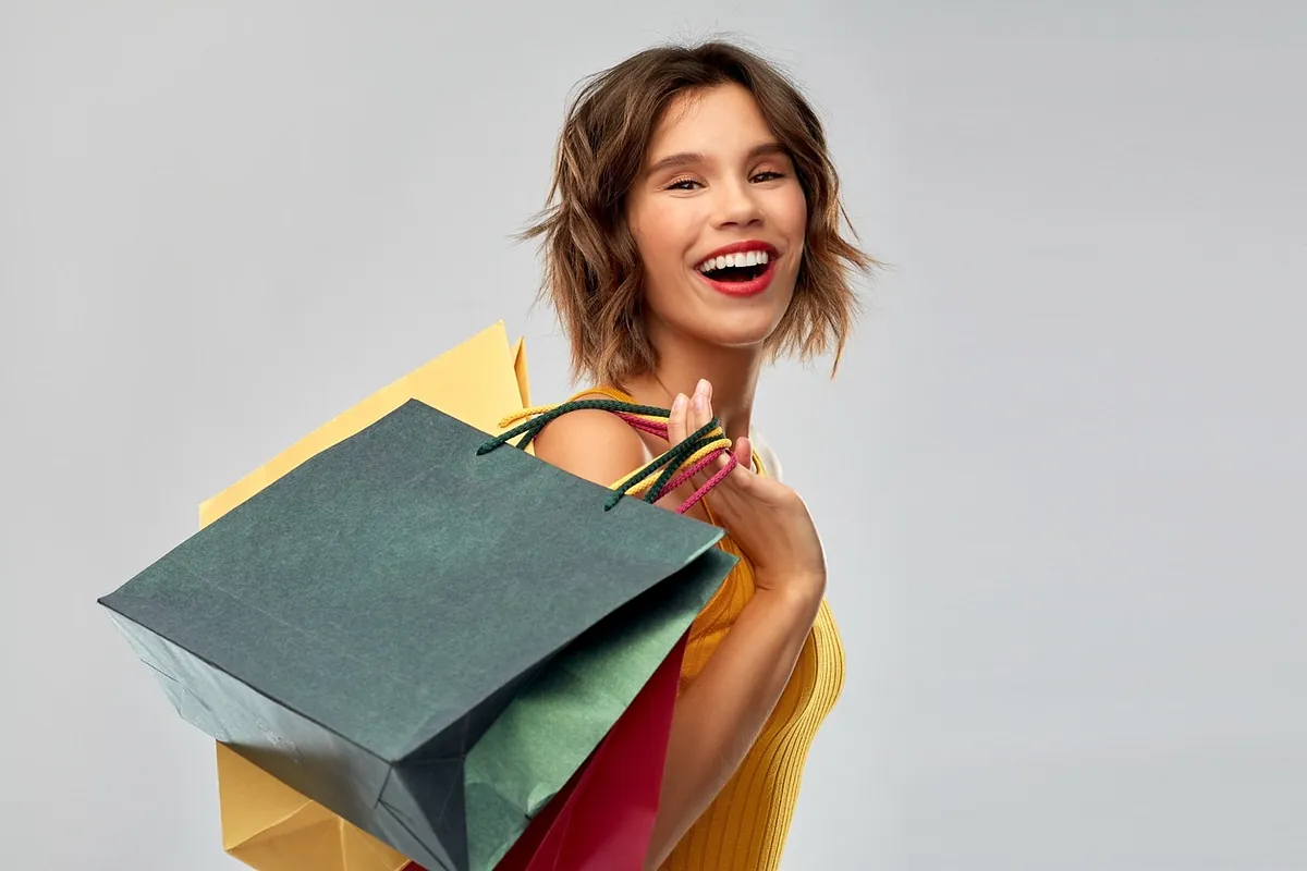 mujer sonriente con bolsas en la mano y fondo gris
